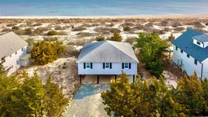 A beachfront property with a house, a covered patio, and a sandy beach in the background.