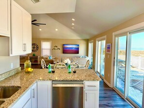 Uma cozinha moderna com bancada de granito, máquina de lavar louça Bosch e área de jantar vista para a praia.