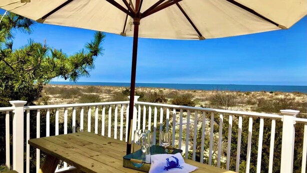 A wooden deck with a picnic table and umbrella overlooking a beach.