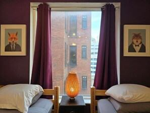 A room with two beds, a table with a lamp, and a window with curtains.