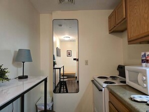 A compact kitchen with a stove, microwave, and cabinets. A mirror reflects the dining area. - Downtown Studio Retreat | Queen Bed + 55” Smart TV (Pittsburgh)
