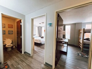 Ein Flur mit Holzboden, ein sichtbares Badezimmer mit Toilette sowie ein Schlafzimmer mit Bett und Fenster.