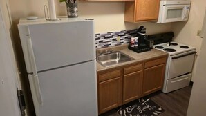 A compact kitchen with a refrigerator, stove, microwave, and wooden cabinets. - Spacious 2BR/2BA Downtown Apt|Clean and Safe| (Pittsburgh)
