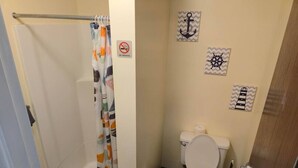 A small bathroom with a shower curtain, toilet, and nautical-themed wall decorations. - Spacious 2BR/2BA Downtown Apt|Clean and Safe| (Pittsburgh)