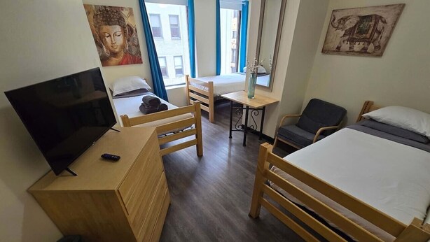 A room with a bed, a desk with a TV, a chair, a small table, and a window with curtains. - Cozy Downtown Pittsburgh Apartment | Smart TV + Wa (Pittsburgh)