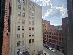 A multi-story building with a brick facade, multiple windows, and a street view with parked cars. - Cozy Downtown Pittsburgh Apartment | Smart TV + Wa (Pittsburgh)