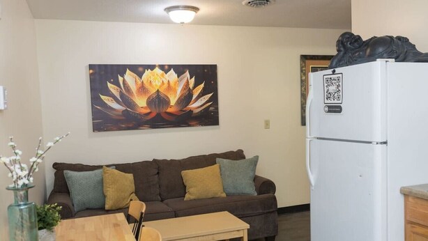 A living room with a brown sofa, a wooden table, a white refrigerator, and a wall-mounted painting of a lotus flower. - Cozy Downtown Pittsburgh Apartment | Smart TV + Wa (Pittsburgh)
