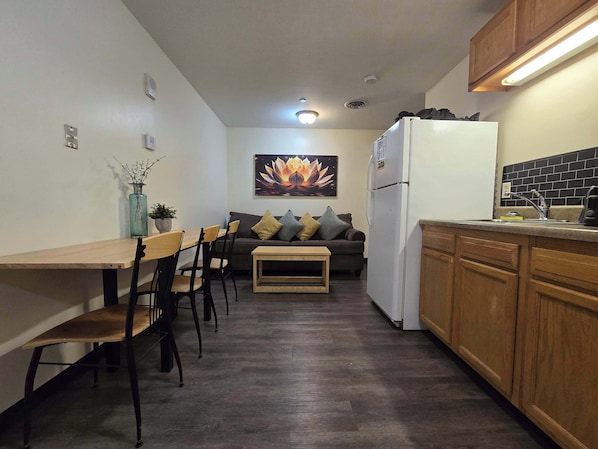 A compact kitchen with a dining area, a sofa, and a refrigerator.
