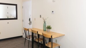A dining area with a wooden table and four chairs, a door, a wall-mounted light switch, and a small potted plant. - Cozy Downtown Pittsburgh Apartment | Smart TV + Wa (Pittsburgh)