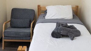 A single bed with a wooden frame, a gray chair, and a wall-mounted artwork of an elephant. - Cozy Downtown Pittsburgh Apartment | Smart TV + Wa (Pittsburgh)