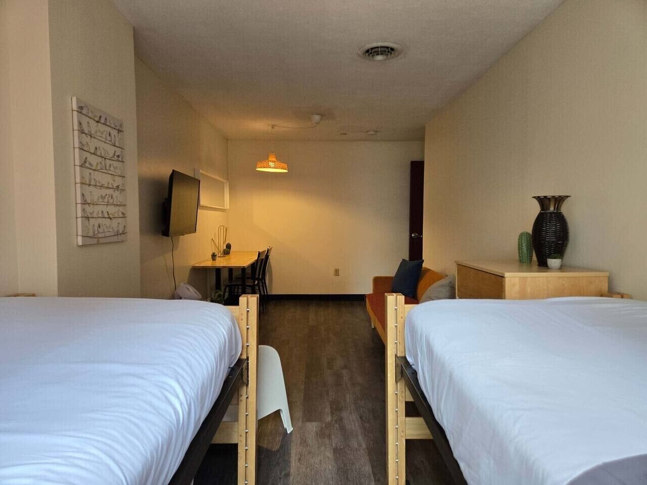 A room with two single beds, a small table, a chair, a TV, and a decorative vase.
