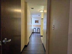 A hallway with a wooden door on the left, a light switch on the right, and a small stool in the distance.
