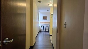 A hallway with a wooden door on the left, a light switch on the right, and a small window at the end.