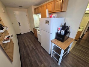Une cuisine avec des meubles de rangement en bois, un réfrigérateur blanc, une machine à café et un four à micro-ondes posés sur un plan de travail en bois.