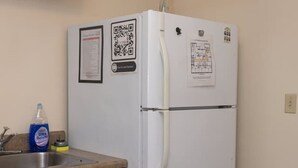 A kitchen with a white refrigerator, wooden cabinets, a stainless steel sink, and a QR code on the refrigerator. - Large Private Downtown Apartment | 2BR + 2BA + 60” (Pittsburgh)