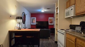 A compact kitchen with a microwave, stove, and toaster. There is a dining area with a table and chairs. The room has red walls and a ceiling light. - Large Private Downtown Apartment | 2BR + 2BA + 60” (Pittsburgh)