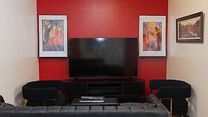 A living room with a large flat-screen TV, black leather sofa, and framed artwork on the walls. - Large Private Downtown Apartment | 2BR + 2BA + 60” (Pittsburgh)