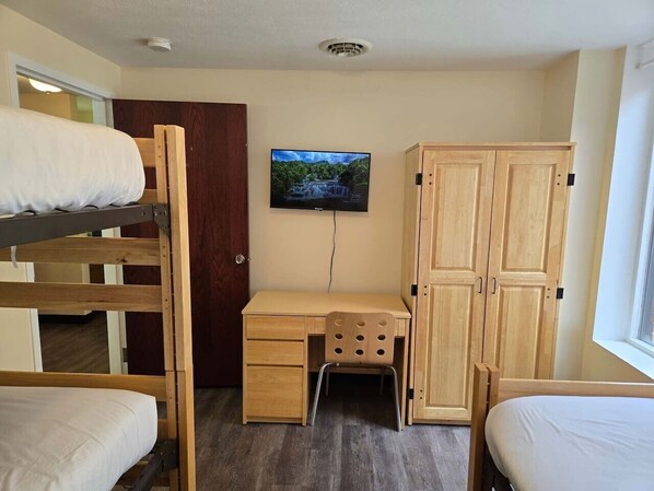 Une chambre avec des lits superposés, un bureau, une télévision et des armoires en bois.