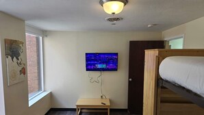 A room with a bed, a television mounted on the wall, and a small wooden table. - Large Private Downtown Apartment | 2BR + 2BA + 60” (Pittsburgh)