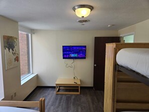 A room with a bed, a television mounted on the wall, and a small wooden table.