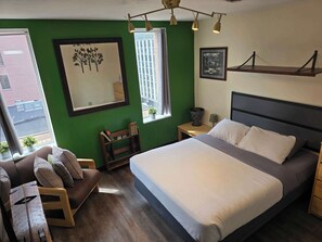 Une chambre à coucher comprenant un lit, une chaise, une table de chevet, une fenêtre et une étagère fixée au mur.