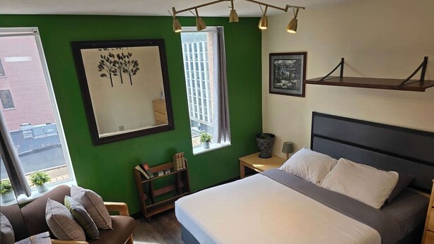 Een hotelkamer met een bed, een bank, een nachtkastje, een raam met uitzicht en een groene wand.