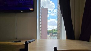 A room with a desk, a chair, a TV mounted on the wall, and a view of a building outside.