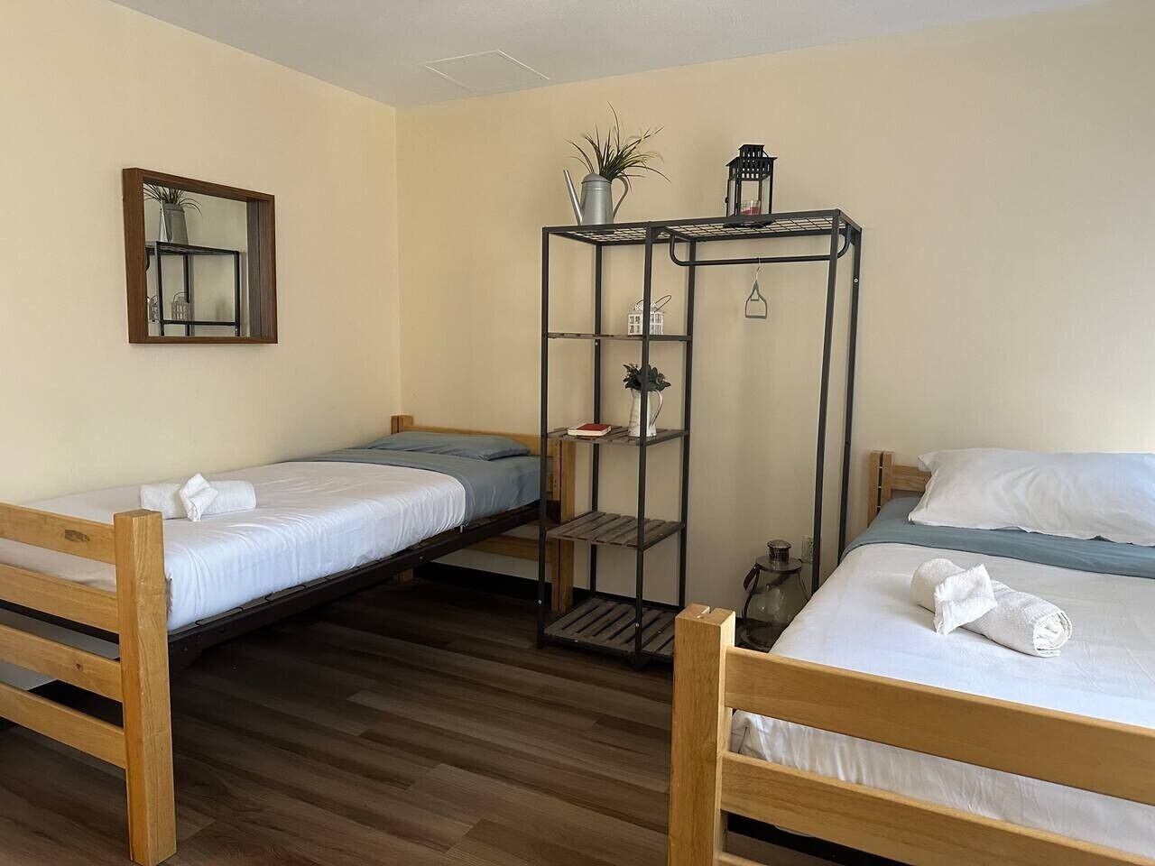 Een kamer met twee houten stapelbedden, een metalen plankenwand met planten, een spiegel en een kleine tafel.