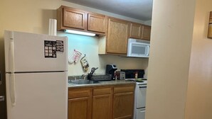 A kitchen with wooden cabinets, a white refrigerator, a microwave, and a stove. - 2BR 2BA Downtown Apt | Spacious + Walkable (Pittsburgh)