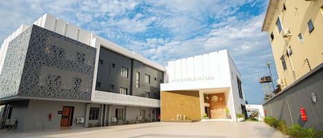 A hotel with a modern facade, a spacious courtyard, and a clear blue sky.