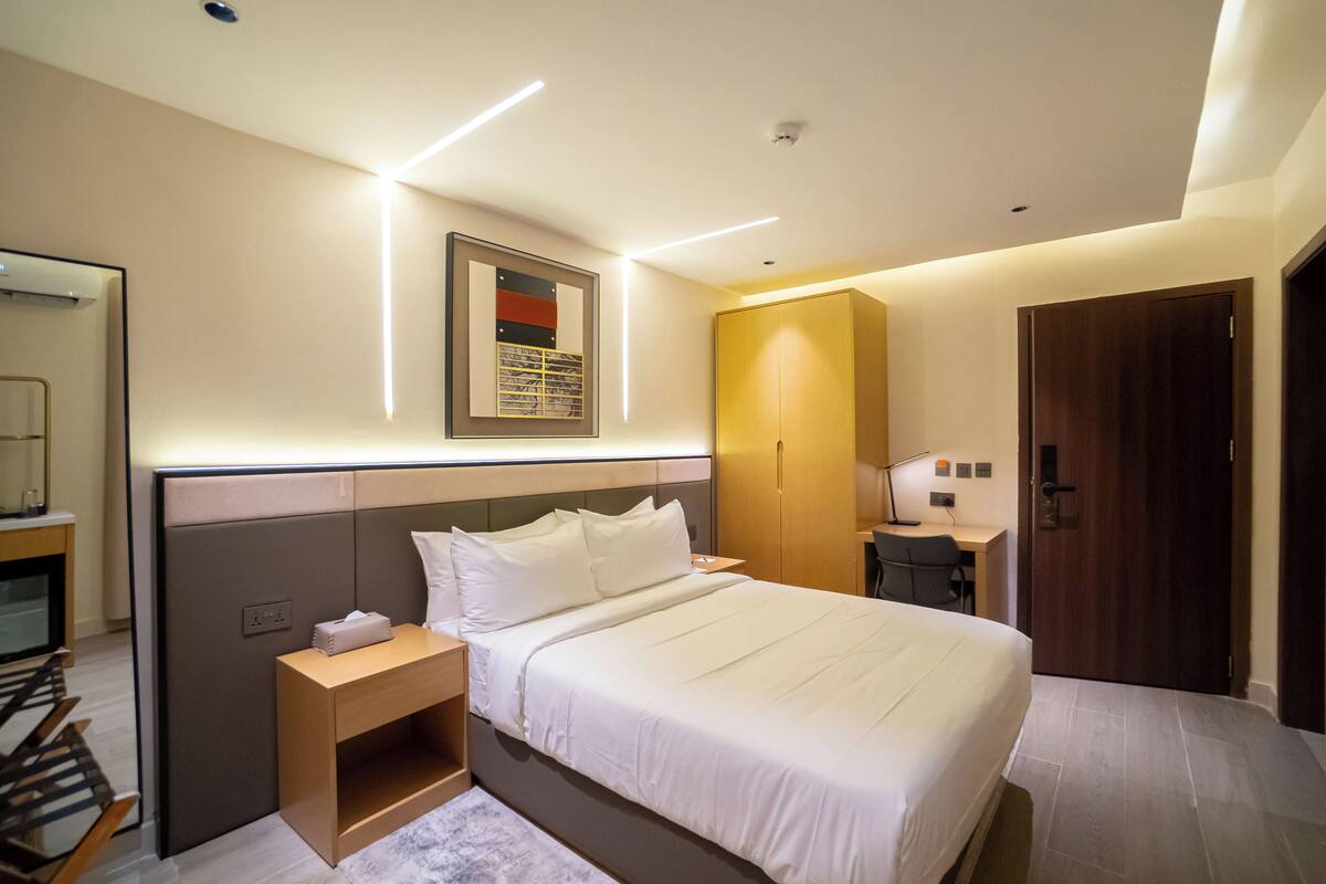 Une chambre d’hôtel moderne avec un lit bien fait, une table de chevet avec une lampe, un bureau et une armoire.