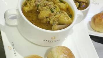 Una bandeja con comida, incluyendo un tazón de sopa, dos panes y un blíster de pastillas.