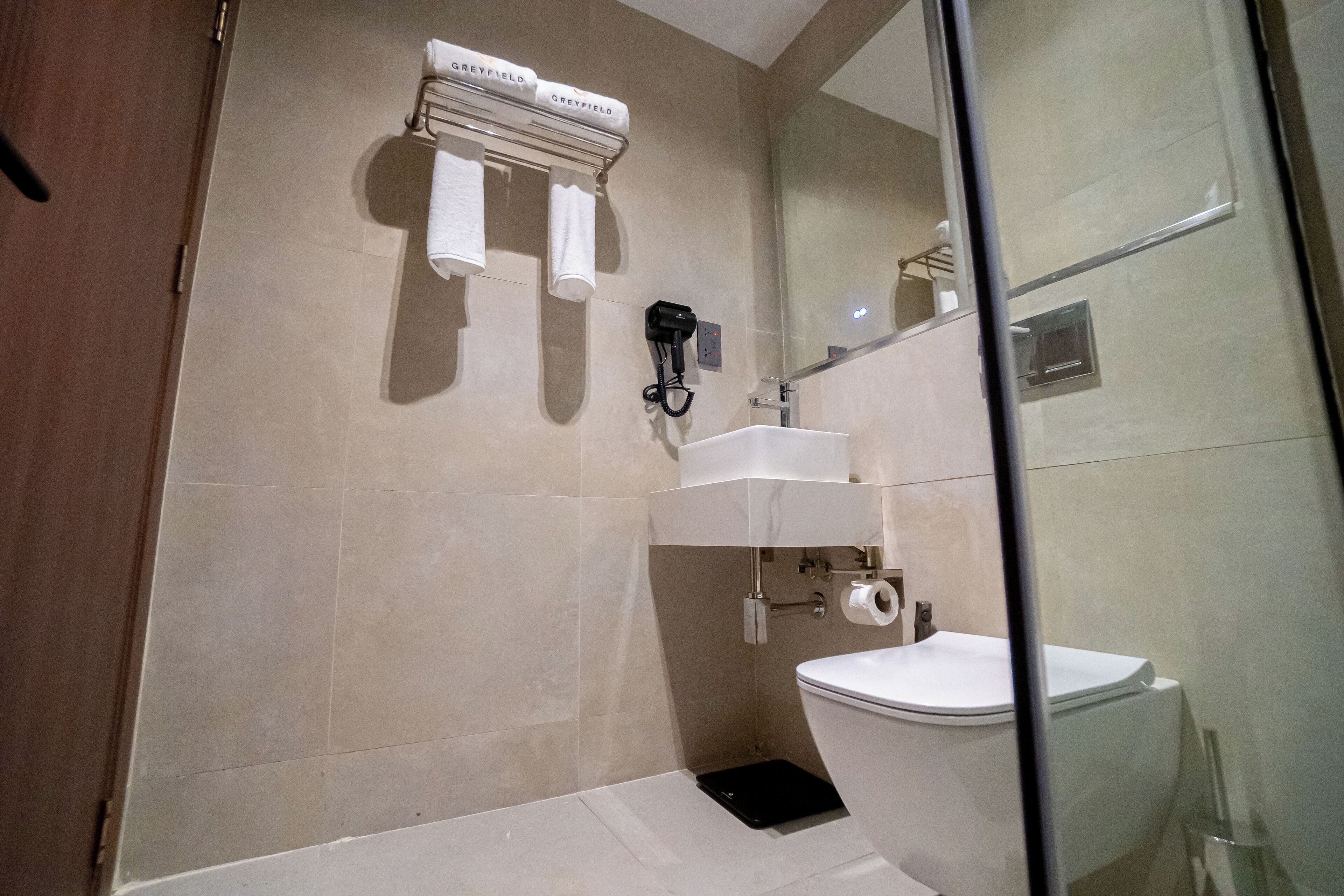 Une salle de bain moderne avec une douche à parois de verre, des toilettes blanches et un porte-serviettes fixé au mur.