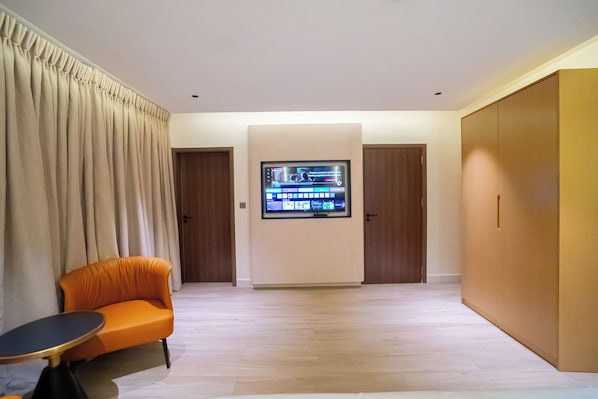 A modern living room with a sofa, a small table, a flat-screen TV mounted on the wall, and a wooden wardrobe.