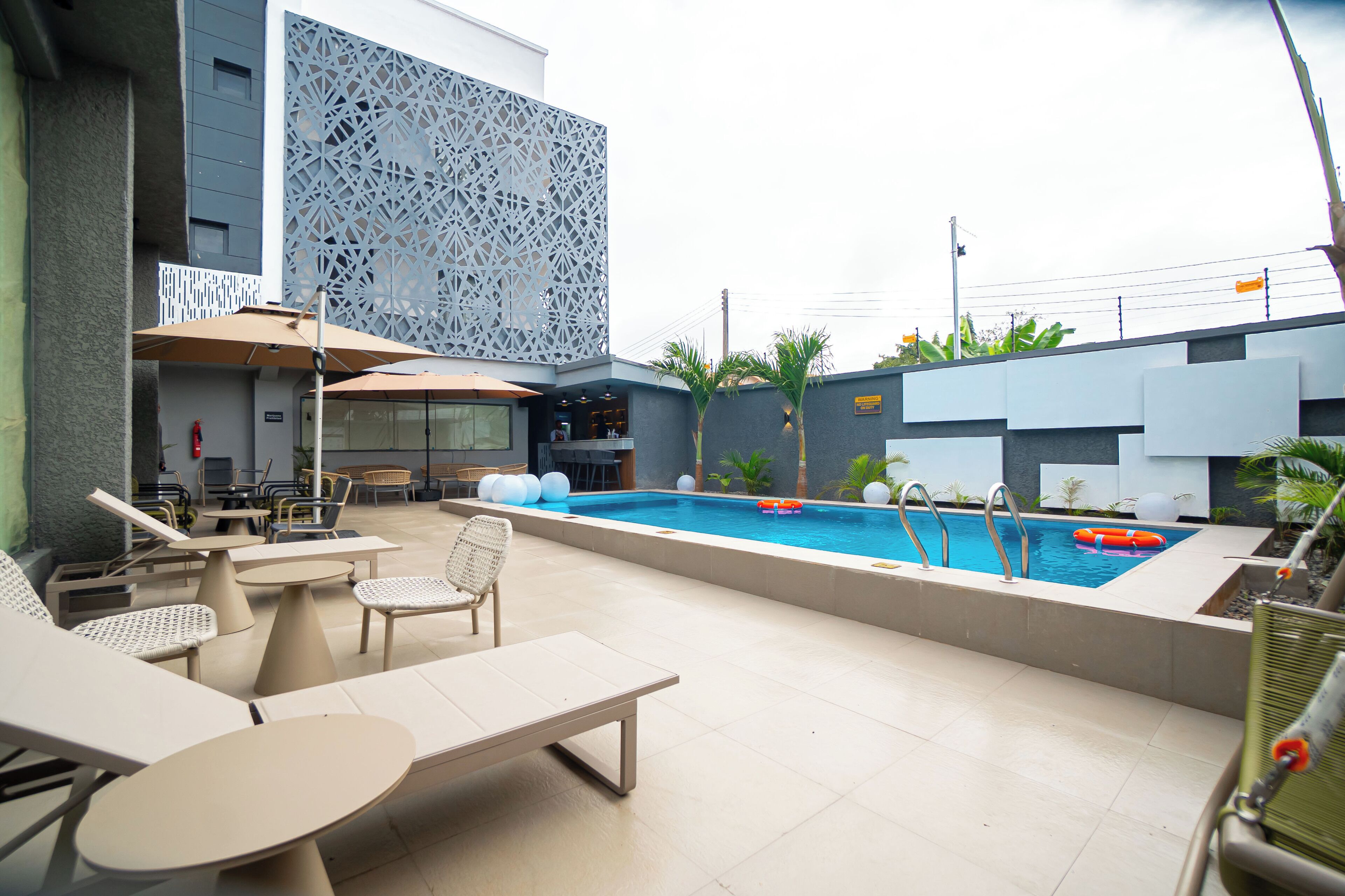An outdoor pool area with lounge chairs, a table, and a decorative wall.