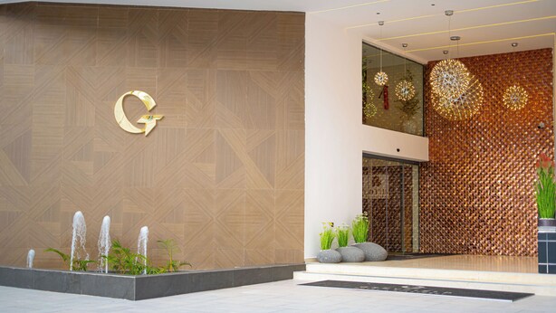 Entrada de un edificio moderno con un diseño geométrico en la pared, un llamativo logo 'G', un elemento de agua y una pared decorativa con patrones circulares.