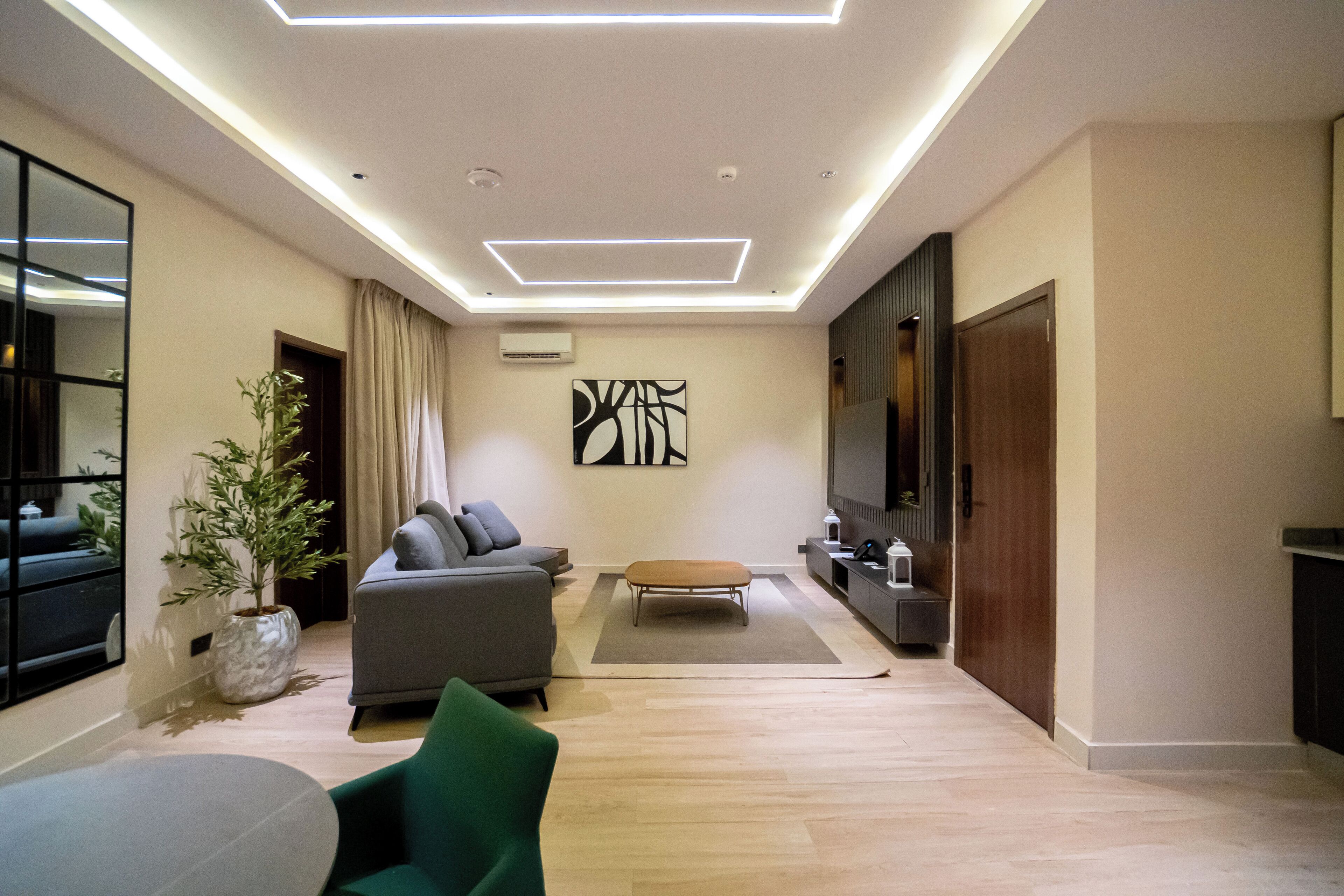 A modern living room with a sofa, a green chair, a coffee table, and a potted plant.