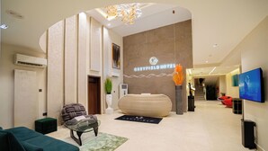 Un moderno vestíbulo de hotel con mostrador de recepción, un sofá, una mesa de centro y un televisor en la pared.