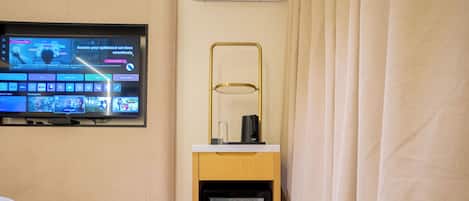A hotel room with a television mounted on the wall displaying various channels and a small refrigerator on a wooden stand.