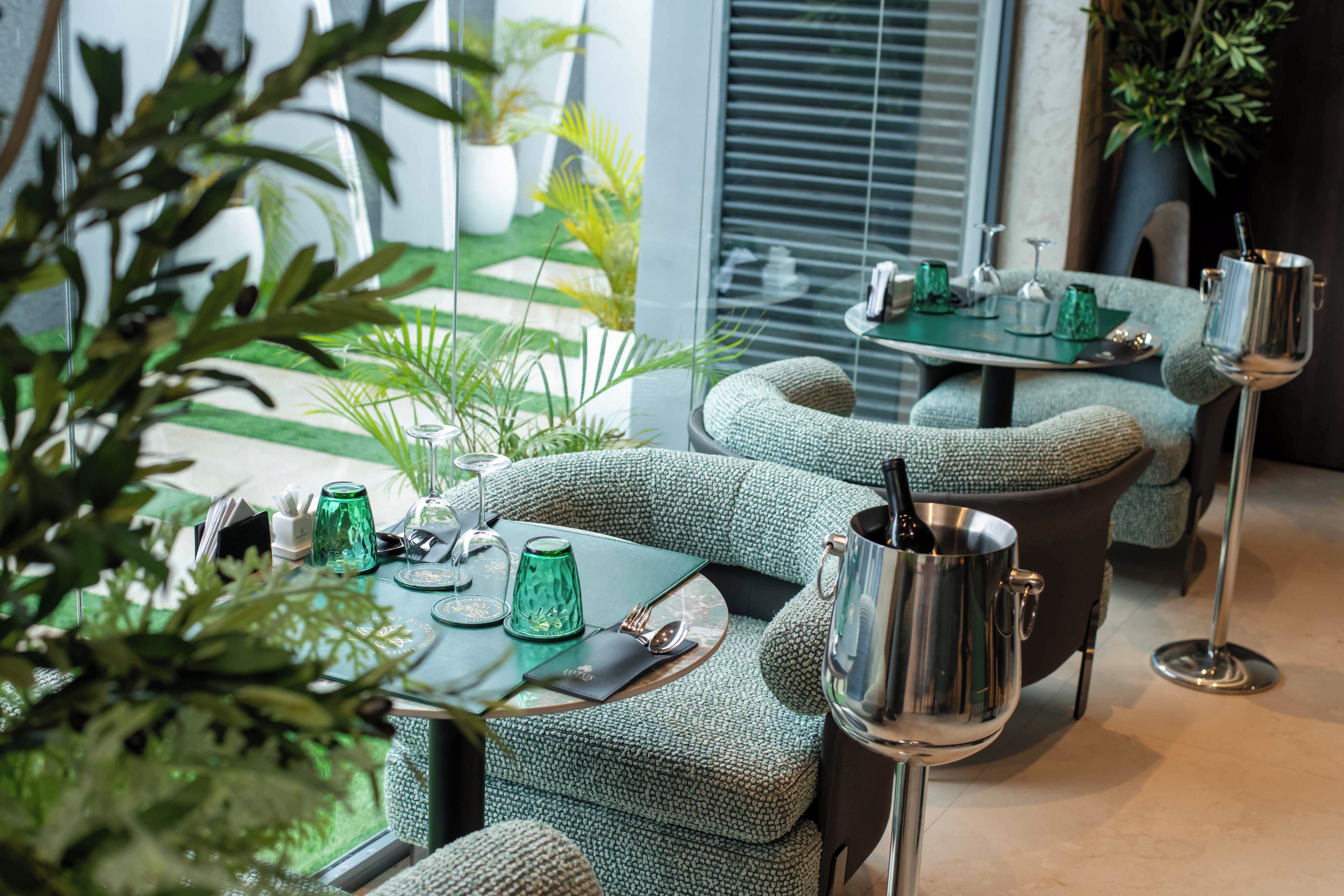 A modern interior with green upholstered seating, a glass table with cutlery, and a metal pot.