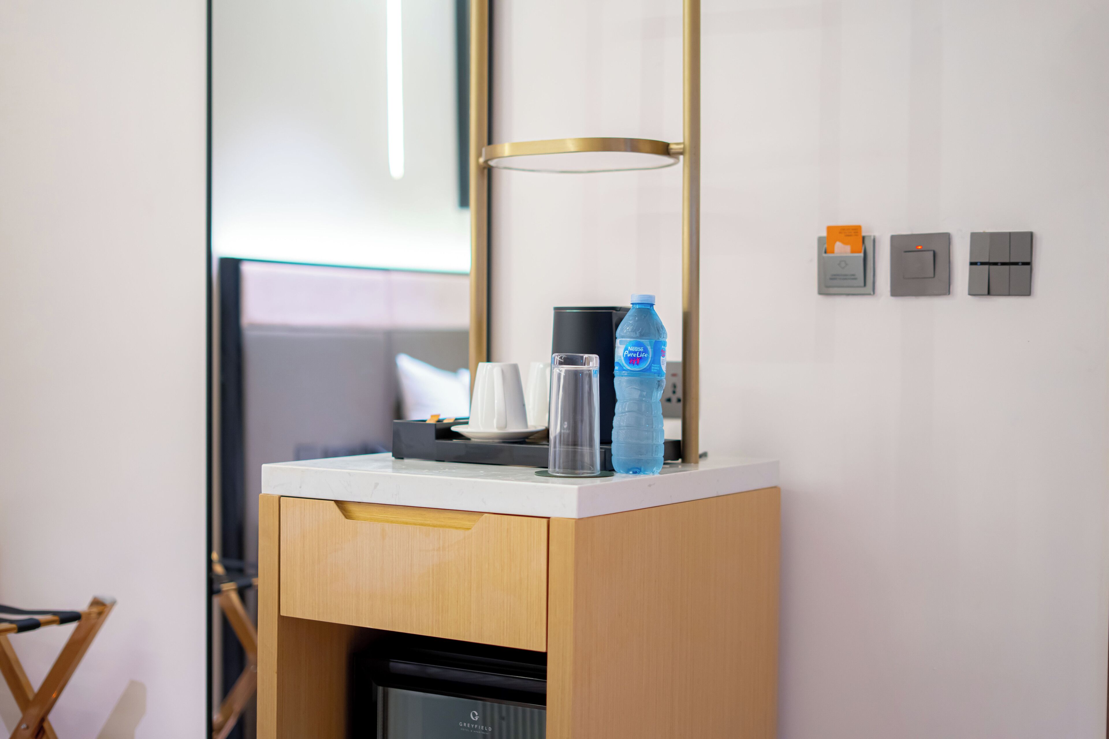 A compact minibar with a water bottle, a coffee maker, and a glass.