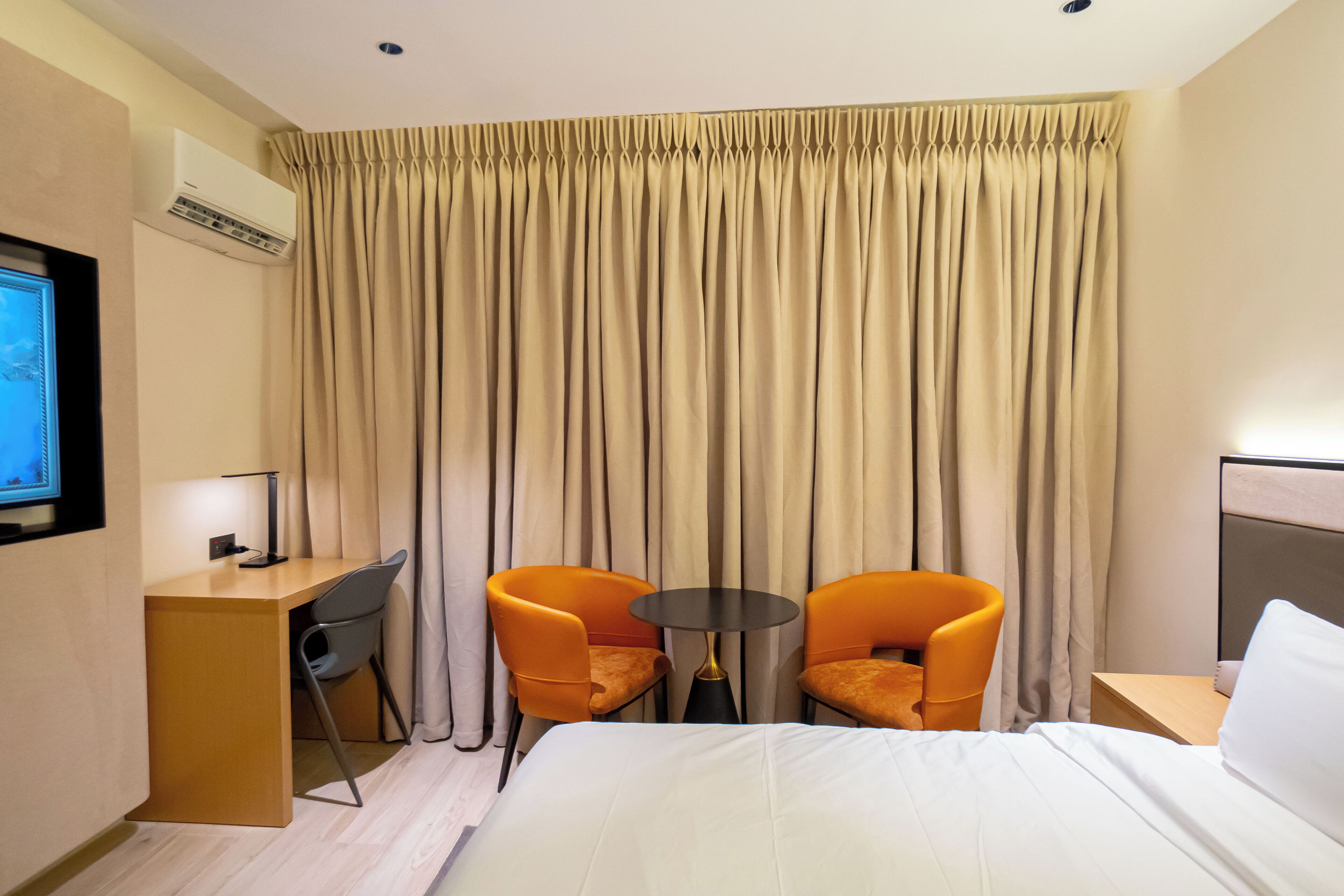 Habitación de hotel con cama, escritorio, dos sillas, una mesita y televisor.