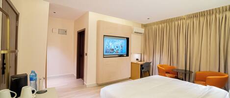 Habitación de hotel con una cama grande, un televisor montado en la pared, un escritorio con una silla y dos sillones naranjas.