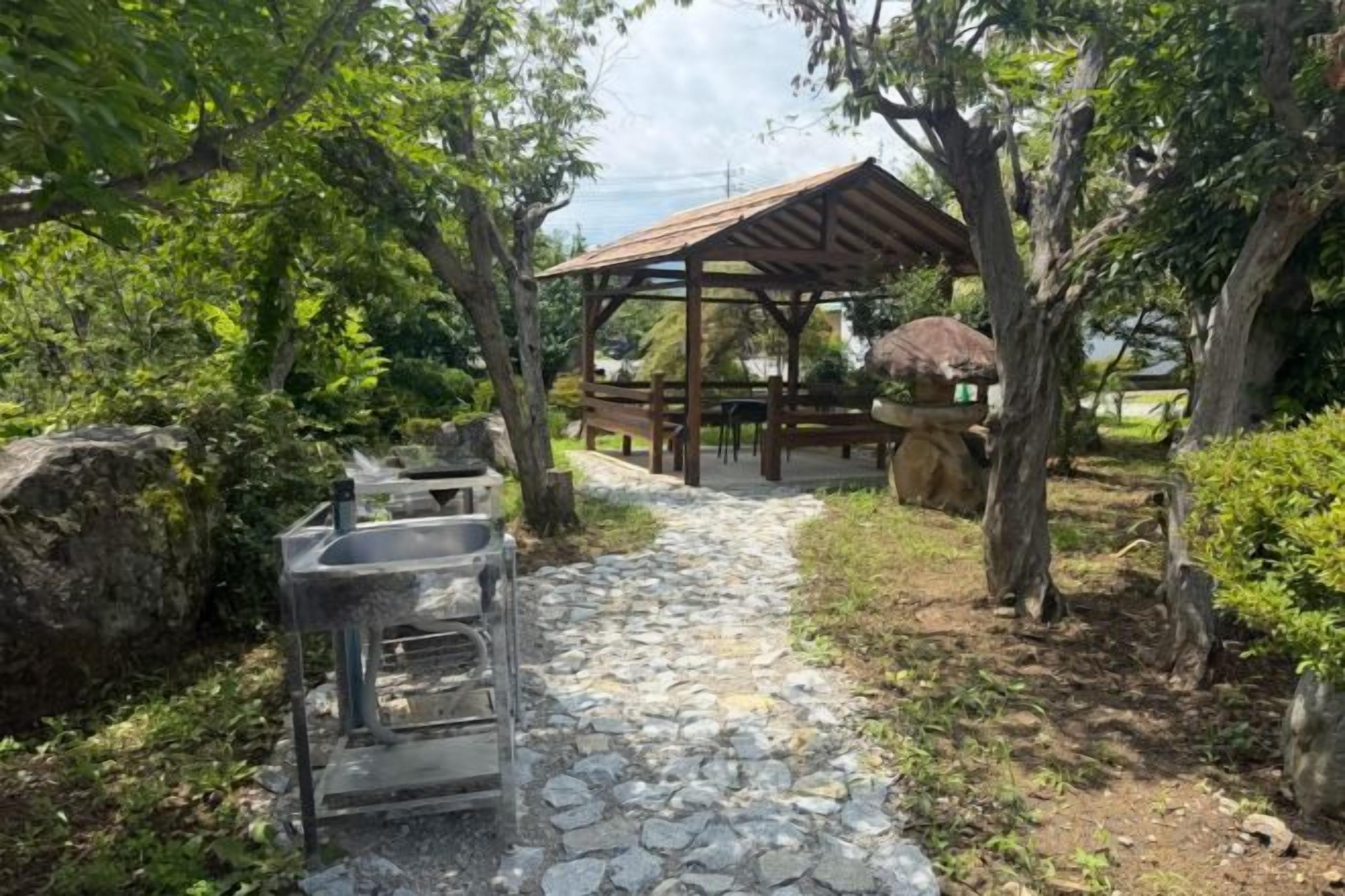 A stone pathway leading to a covered outdoor seating area with a grill and a table.