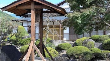 A traditional Japanese building with a wooden structure in the foreground, surrounded by well-maintained bushes and rocks.