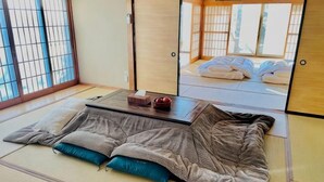 Una habitación con esterillas de tatami, una futón, una mesita con una caja de pañuelos y vistas a una habitación japonesa tradicional a través de un shoji.