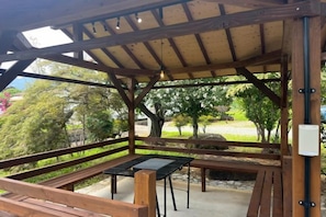 A covered outdoor seating area with benches and a table, surrounded by trees and a view of a park. - KazenoRyoan-Fuga (Koshu)