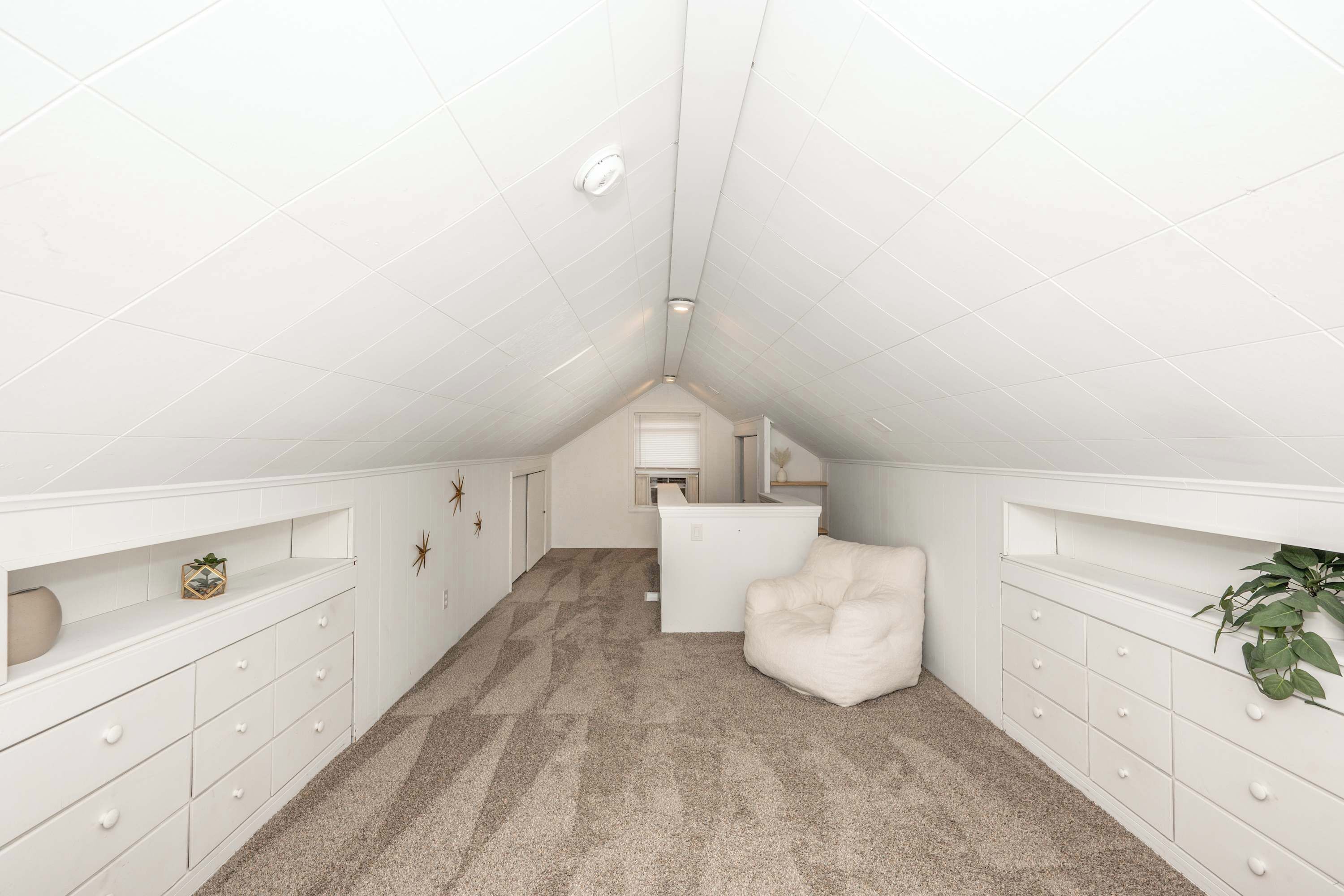 Ein Schlafzimmer im Dachgeschoss mit weißer, geneigter Decke, beigem Teppich, weißem Schminktisch und einem weißen Stuhl.