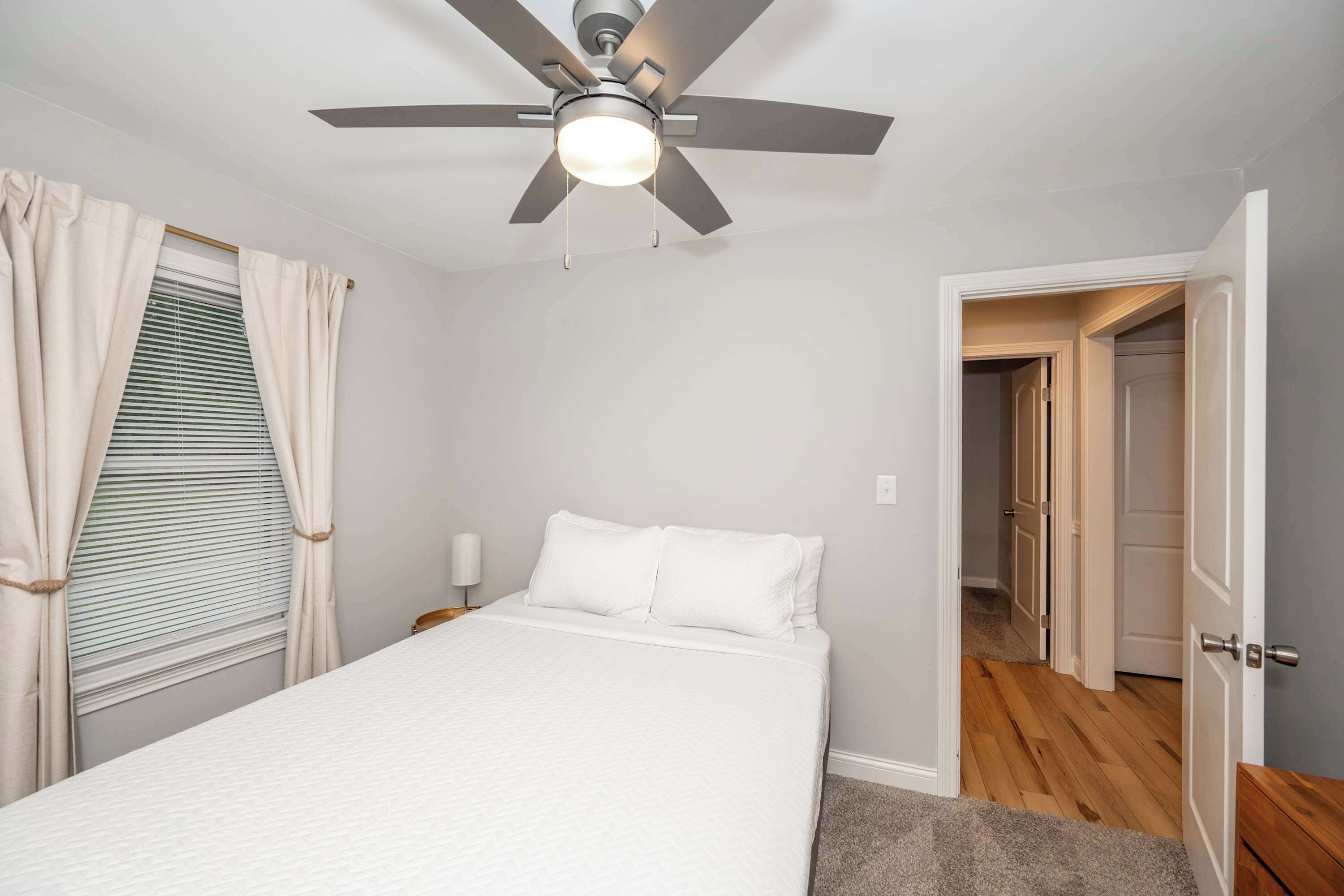 A bedroom with a bed, a ceiling fan, a nightstand, and a door leading to another room.