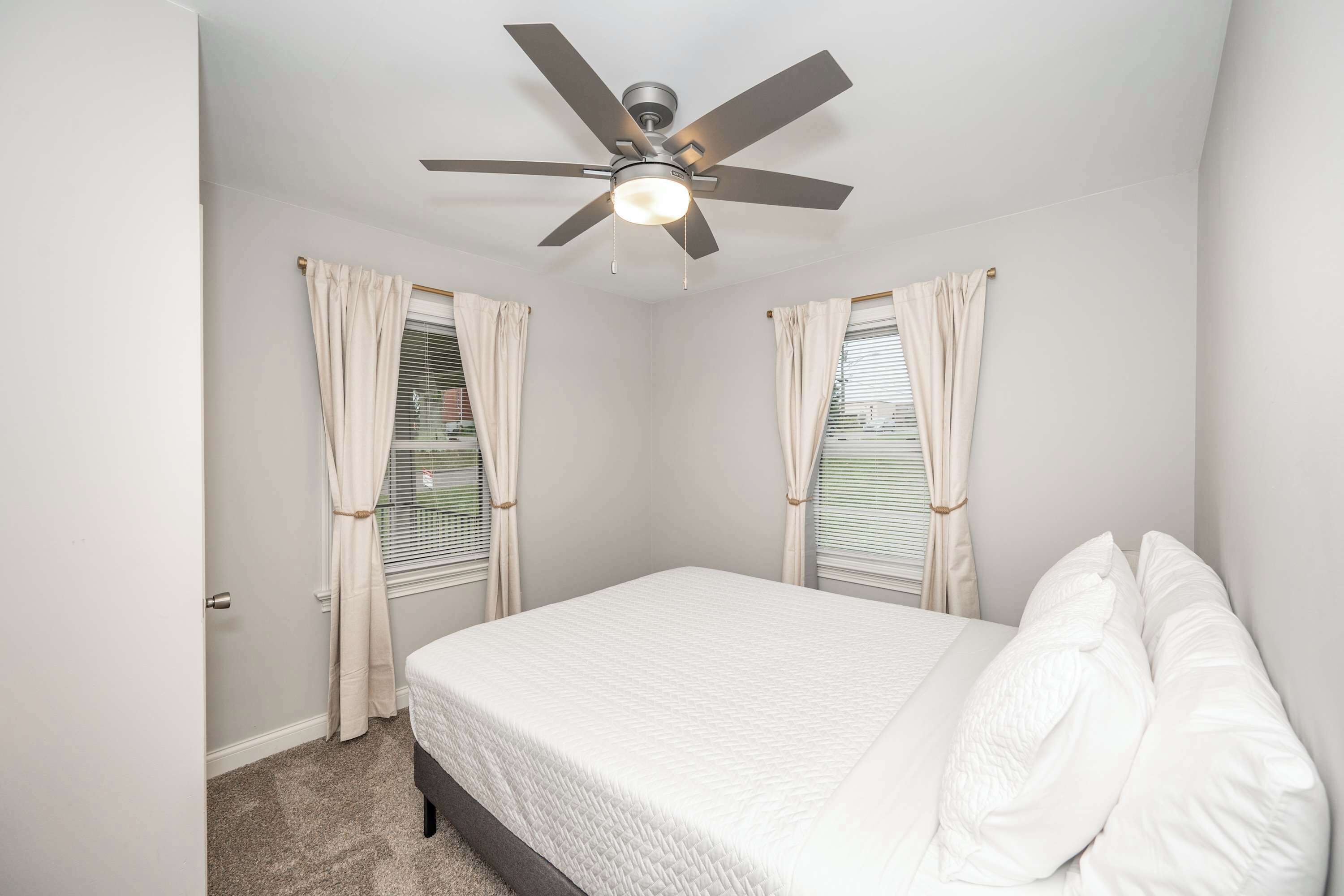 A bedroom with a bed, a ceiling fan, and two windows with curtains.